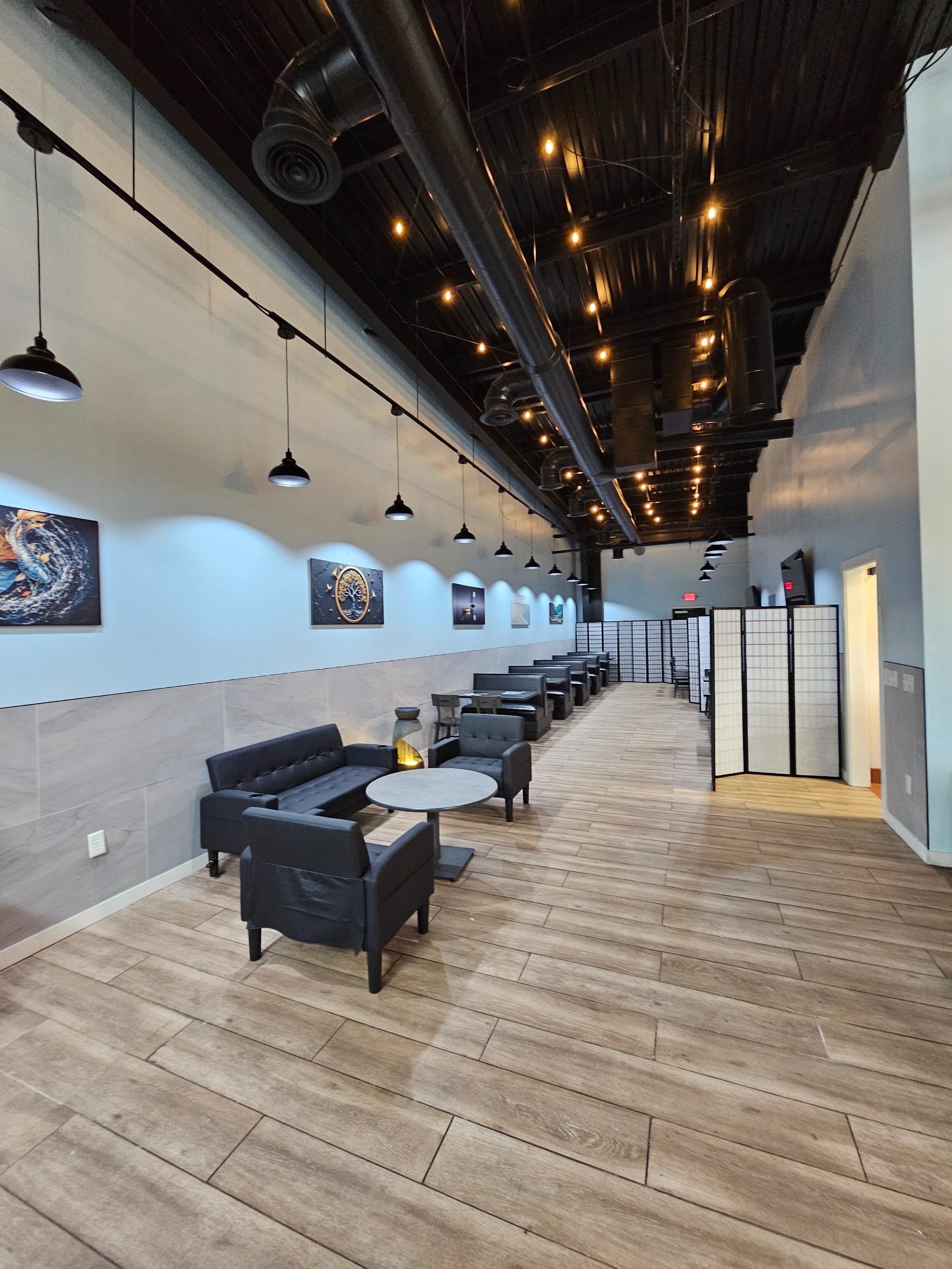 The long dining hall at Osaka Express with booths, lounge seating and hand-painted canvases under a black industrial ceiling