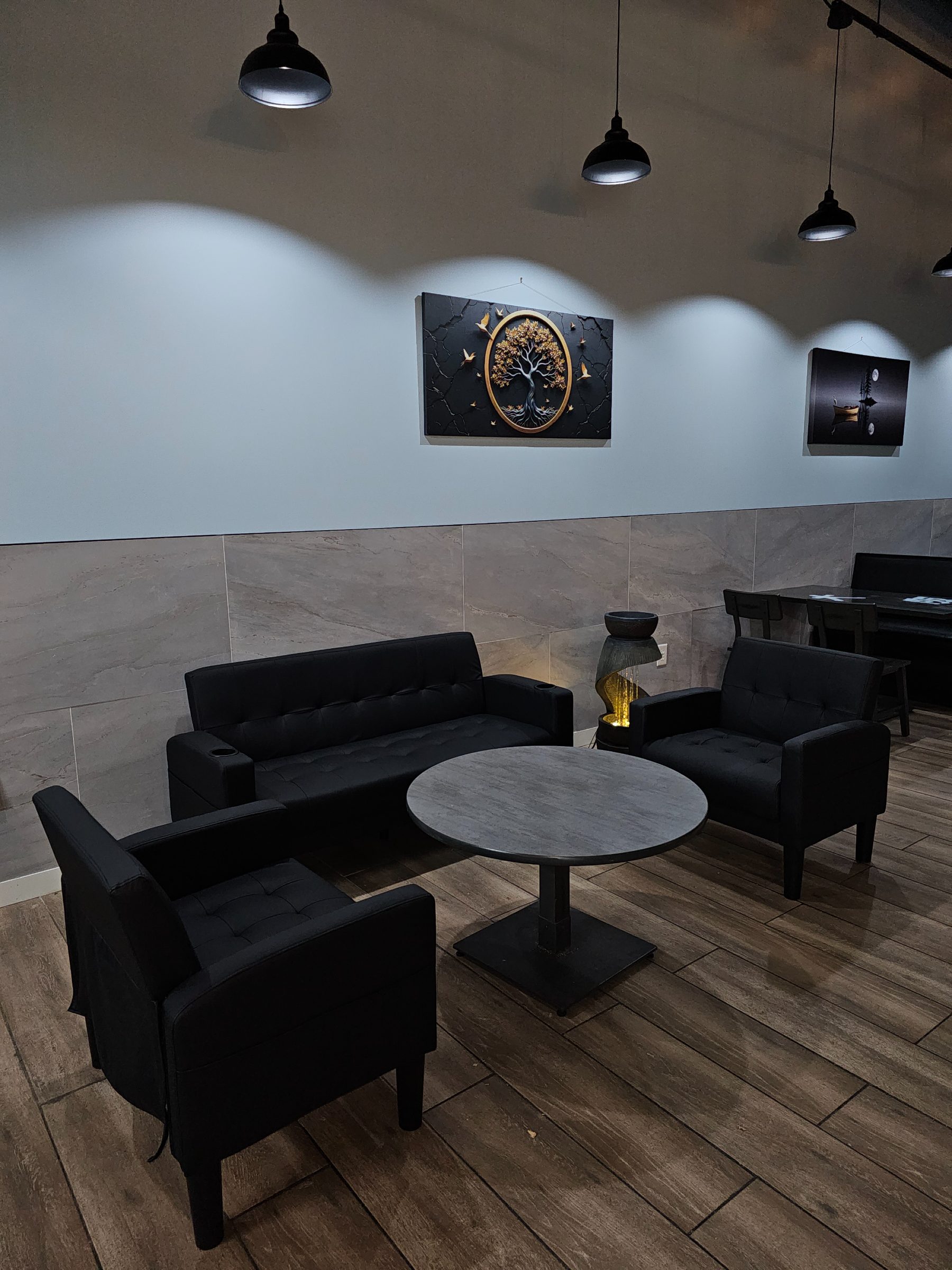 Lounge sofas, armchairs and a round table beneath a gold tree-of-life canvas at Osaka Express